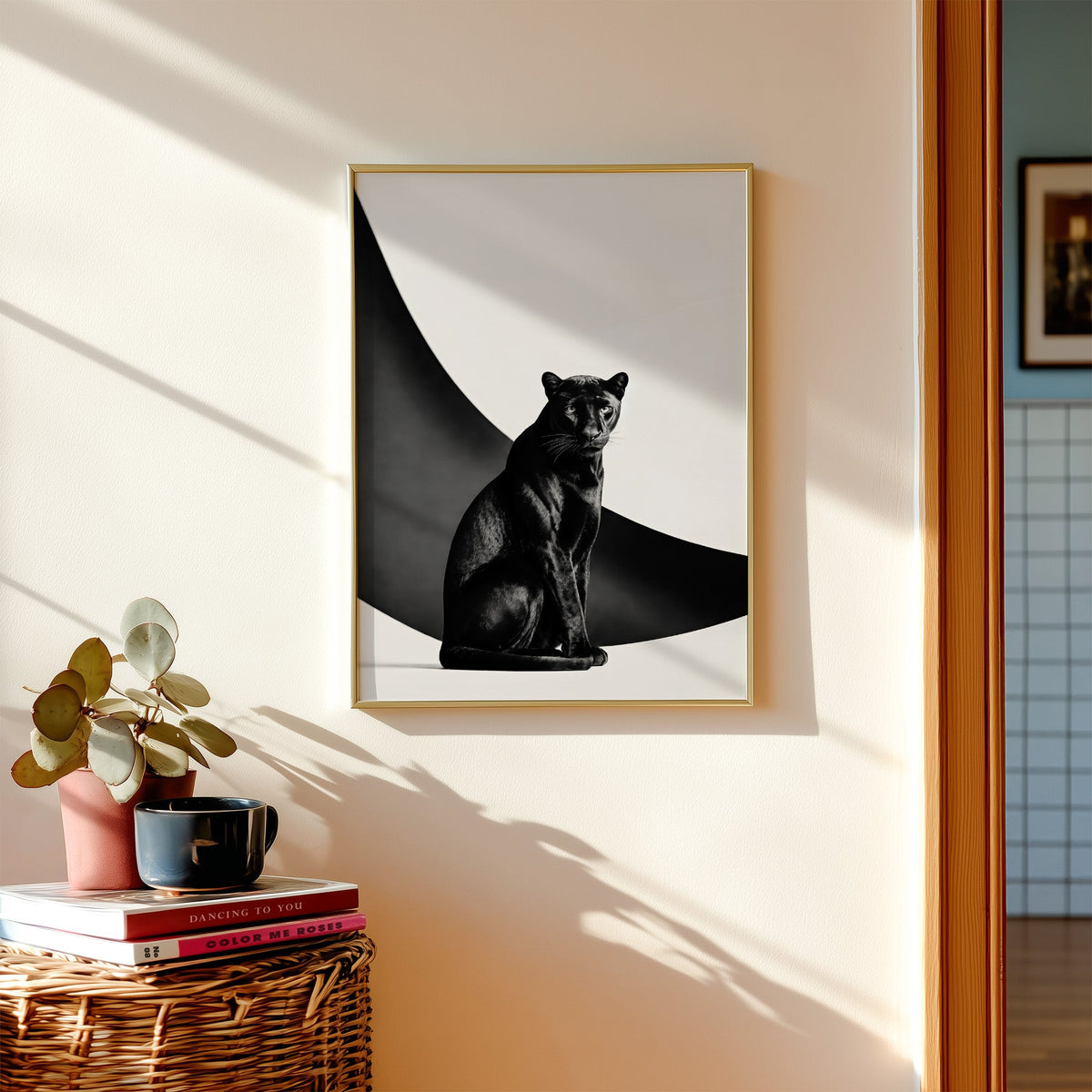 Seated black panther in front of black arc print shown in a gold frame above a wicker basket and stacked books