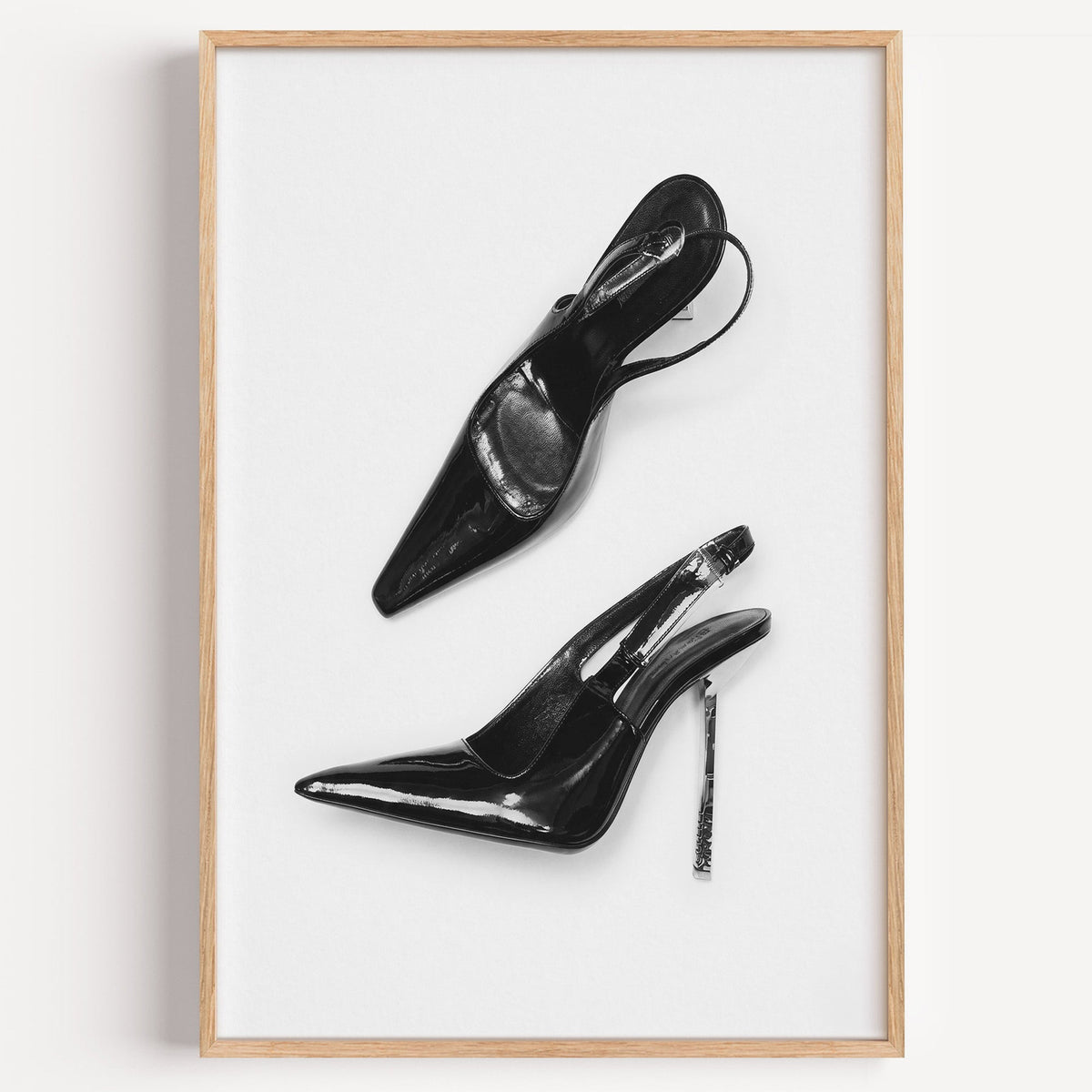 Black patent slingbacks with silver heels print in a light oak frame on a plain white wall