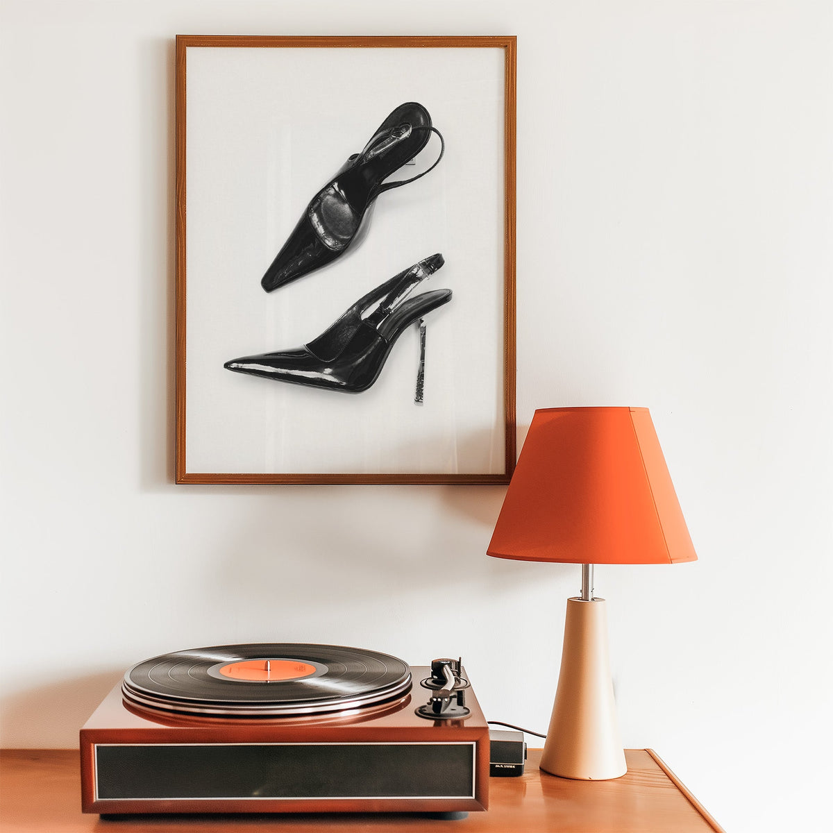 Black patent slingbacks with silver heels print in a walnut frame above a record player and orange lamp