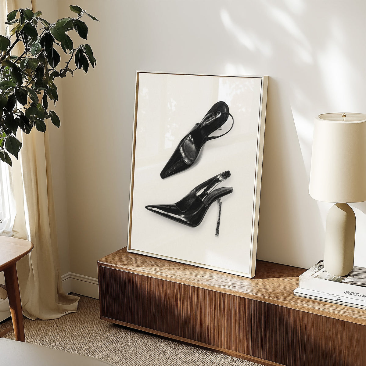 Black patent slingbacks with silver heels print in a white frame on a walnut sideboard beside a ceramic lamp