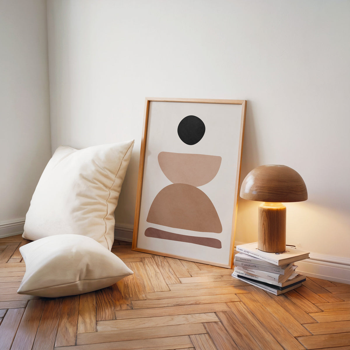 Black pebble and stacked stones mid century print in a light wood frame on a herringbone floor by a wooden mushroom lamp