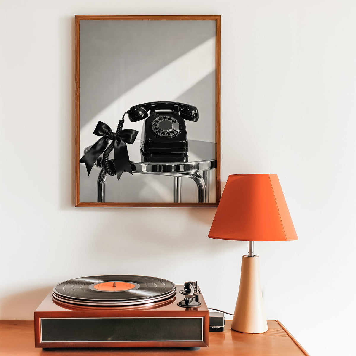 Black rotary phone with satin bow on chrome table print in a walnut frame above a record player and orange lamp