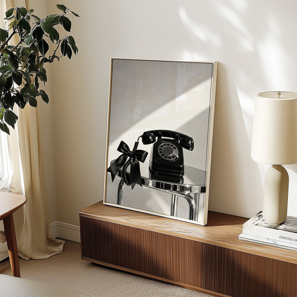 Black rotary phone with satin bow on chrome table print in a white frame on a walnut sideboard beside a ceramic lamp