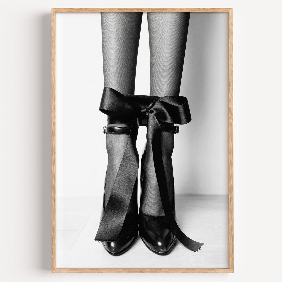 Heels with black satin bows tied at the ankle print in a light oak frame on a plain white wall