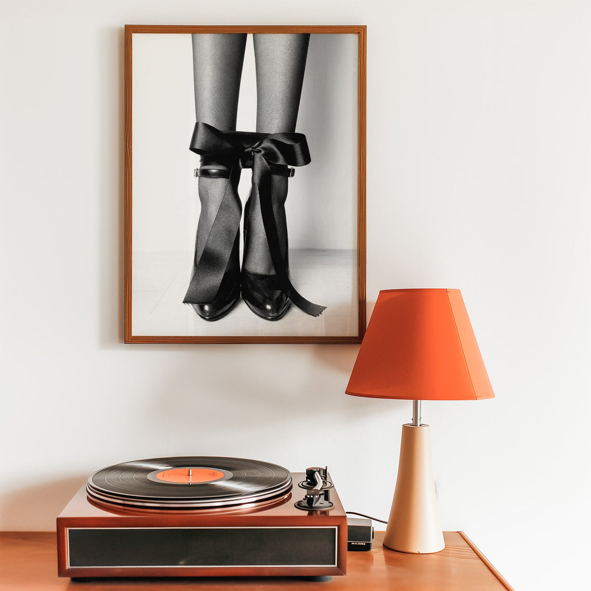 Heels with black satin bows tied at the ankle print in a walnut frame above a record player and orange lamp