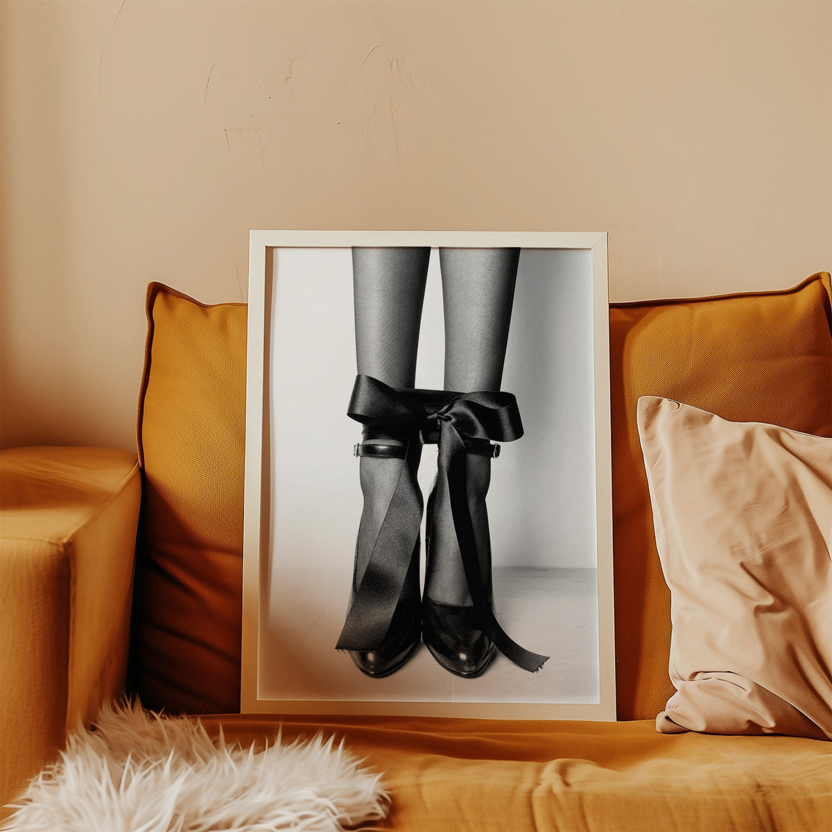 Heels with black satin bows tied at the ankle print in a white frame leaning on a mustard velvet sofa
