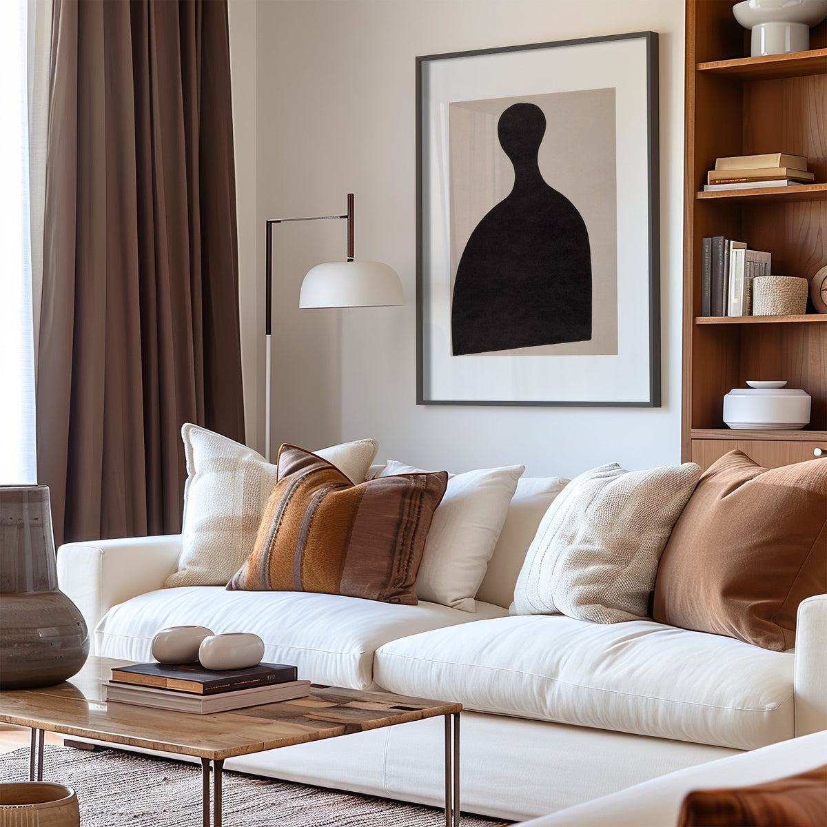 Black silhouette bust on blush panel print in a black frame above a cream sofa with brown striped pillows