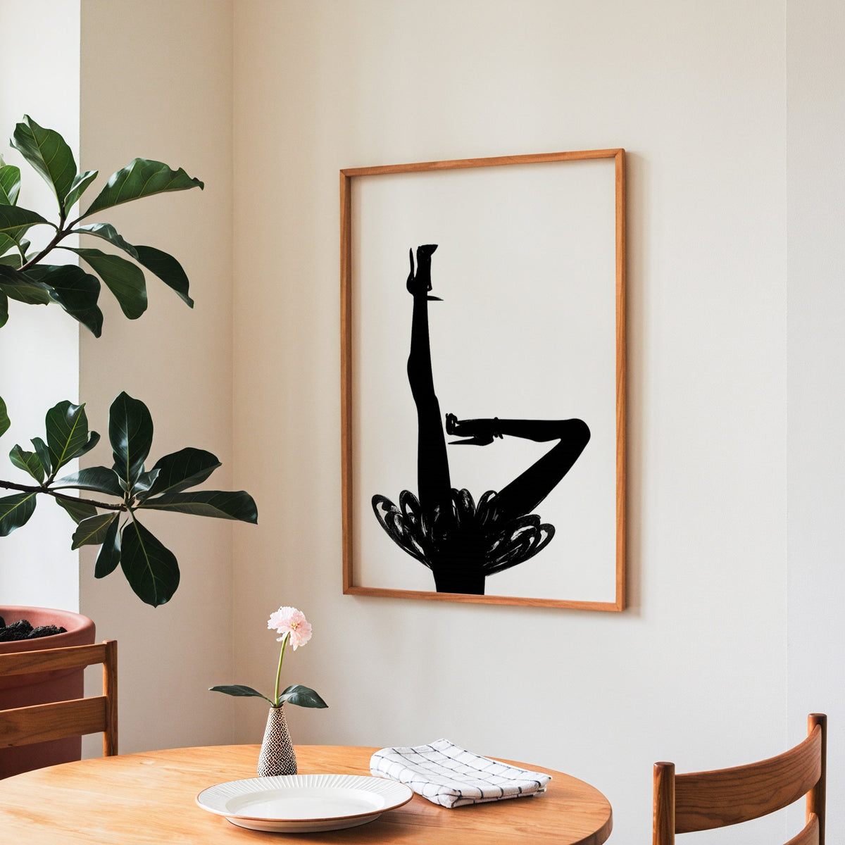 Black silhouette legs in heels with brushstroke skirt print in a teak frame above a round wooden dining table