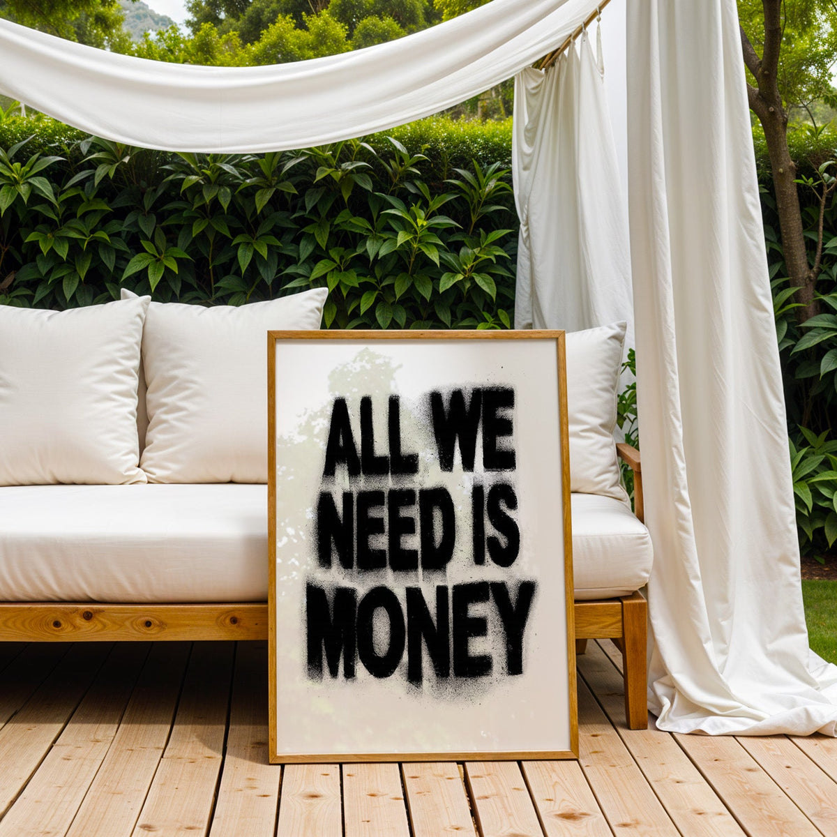 Spray paint lettering money quote print in an oak frame on an outdoor daybed under white drapes