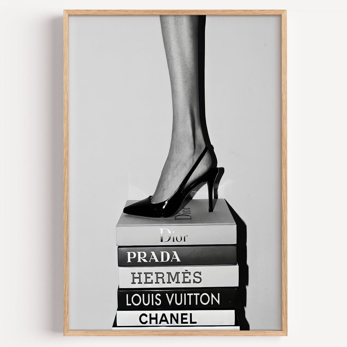 Glossy slingback heel standing on stacked books print in a light oak frame on a plain white wall