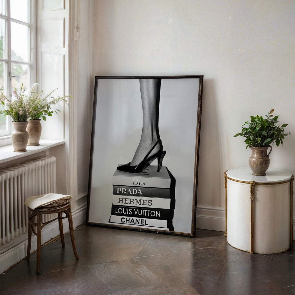Glossy slingback heel standing on stacked books print in a black frame on a dark stone floor beside a white side table