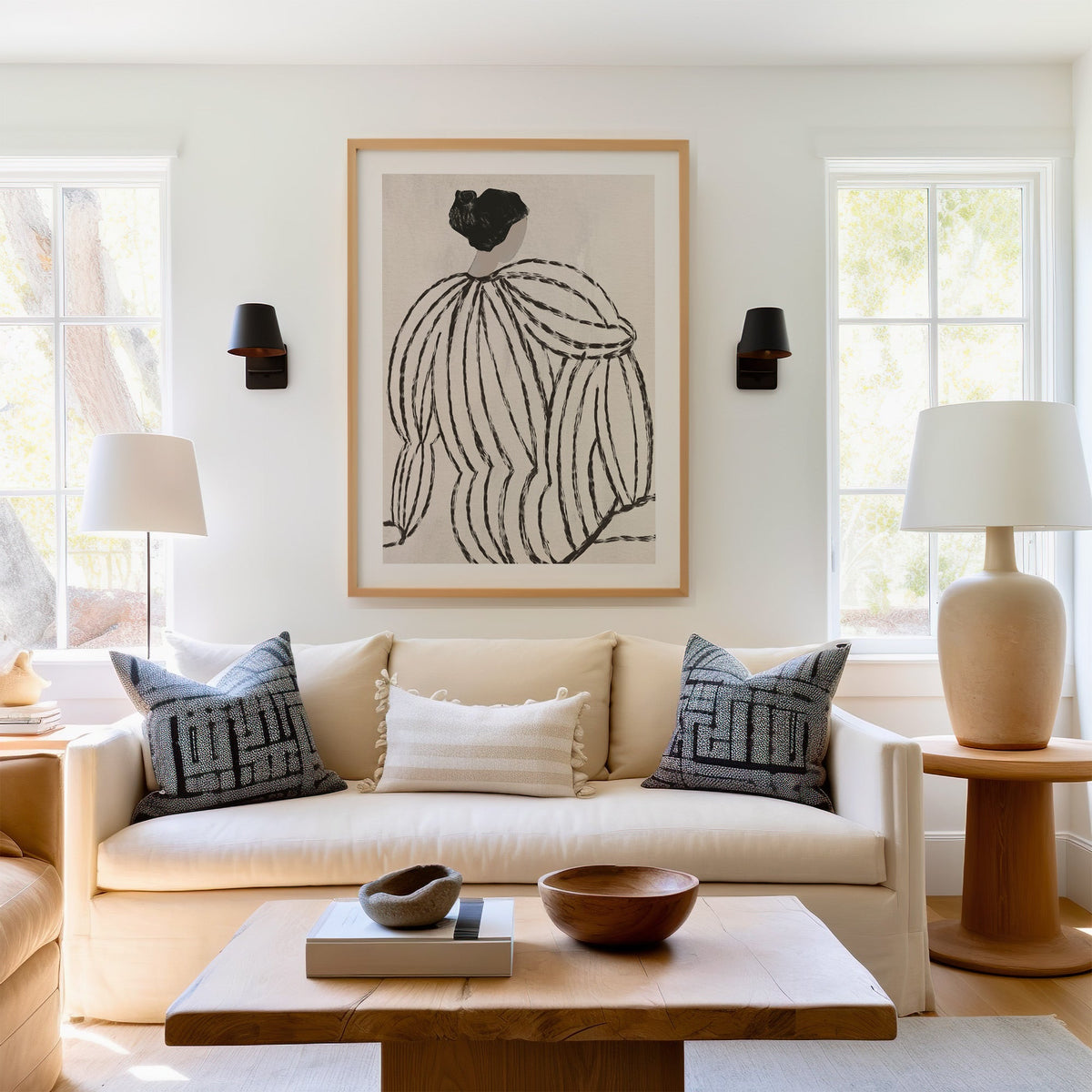 Woman in striped blouse from behind sketch print in a light oak frame above a cream sofa between two black wall sconces