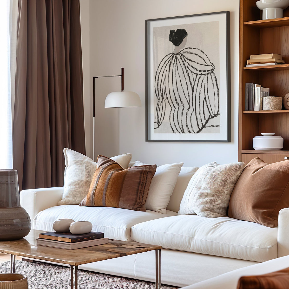 Woman in striped blouse from behind sketch print in a black frame above a cream sofa with brown striped pillows