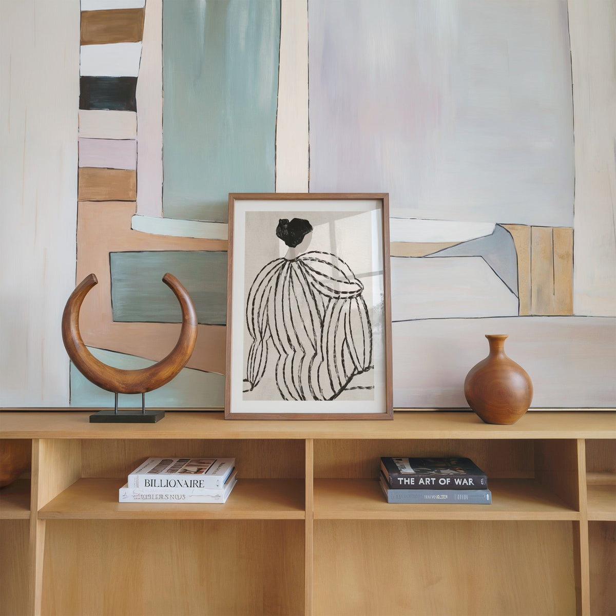 Woman in striped blouse from behind sketch print in a walnut frame on an oak shelf beside a wooden crescent sculpture