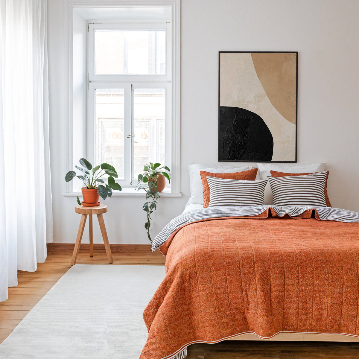 Black and tan textured shapes abstract print in a thin black frame above a bed with a rust orange quilt