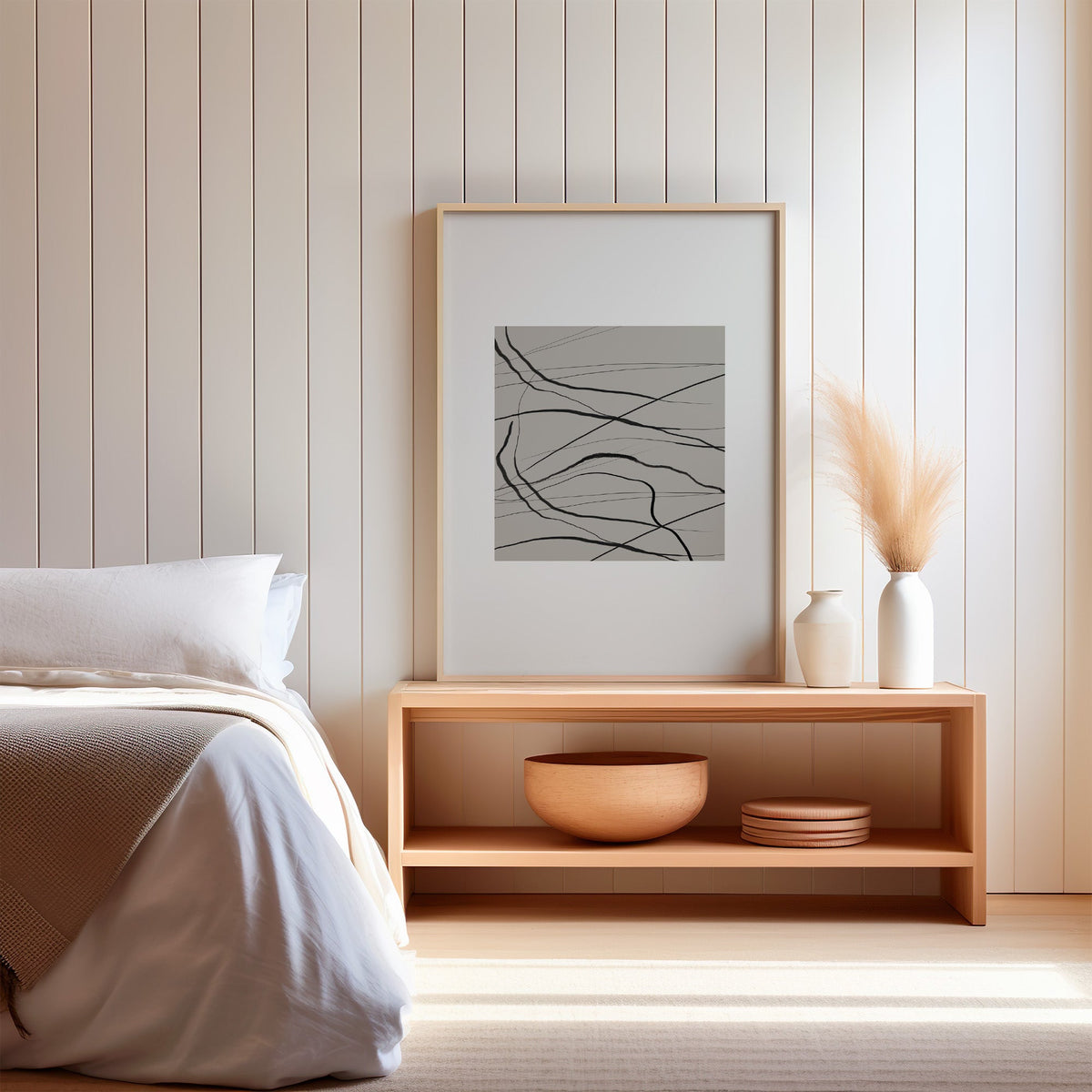 Black tangled lines on taupe square print in a light oak frame on a wood bench by a bed with pampas grass