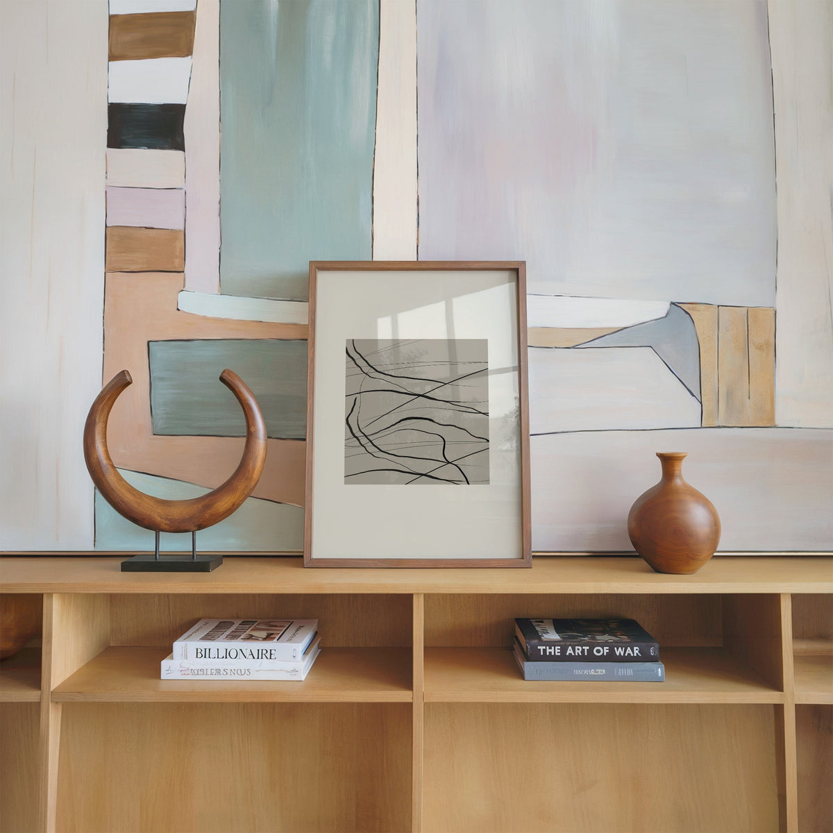 Black tangled lines on taupe square print in a walnut frame on an oak shelf beside a wooden crescent sculpture