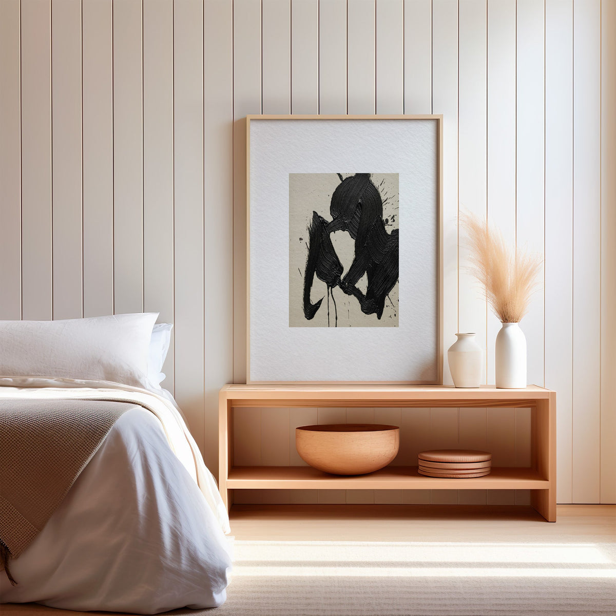 Black calligraphy brushstroke on beige paper print in a light oak frame on a wood bench by a bed with pampas grass