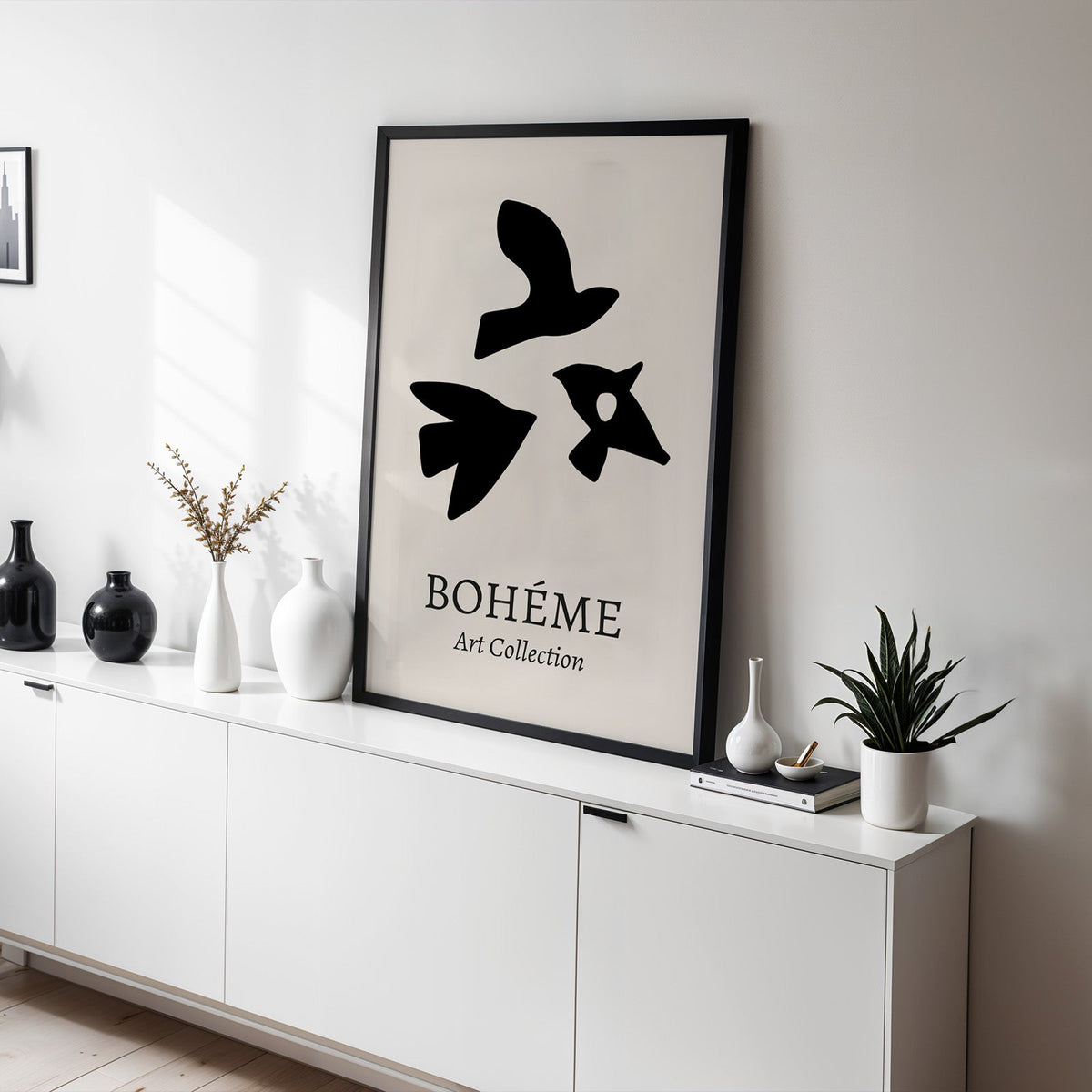 Black three birds cutout abstract print in a black frame leaning on a white sideboard with black and white vases