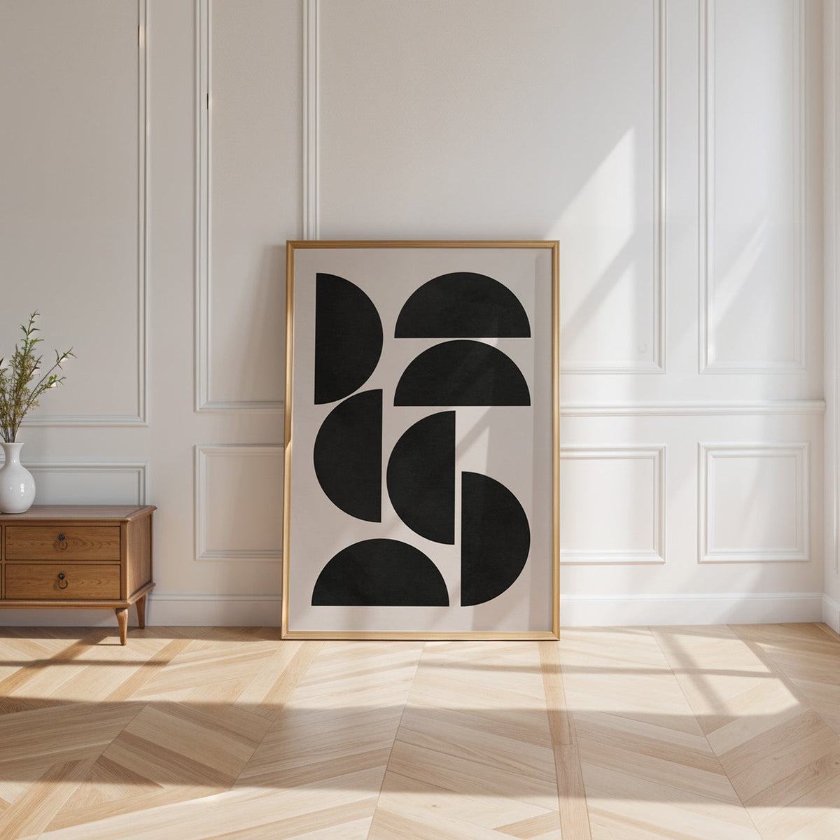 Black tiled half circles mid century print shown in a gold frame leaning on a paneled white wall in sunlight