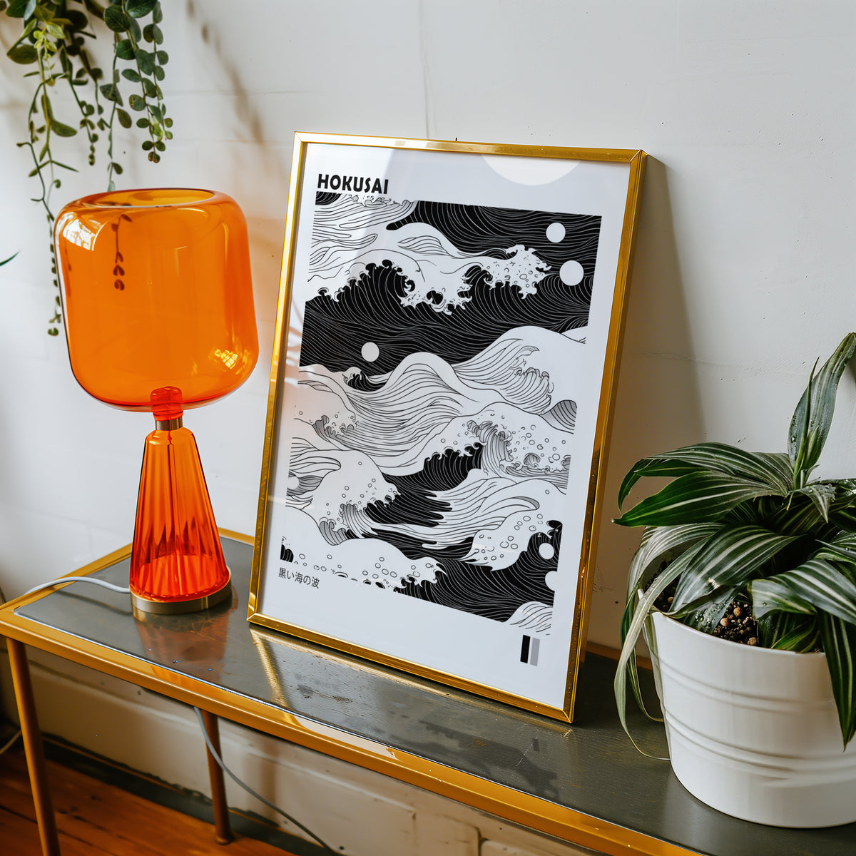 Black sea waves with twin moons print shown in a gold frame on a console beside an orange glass lamp