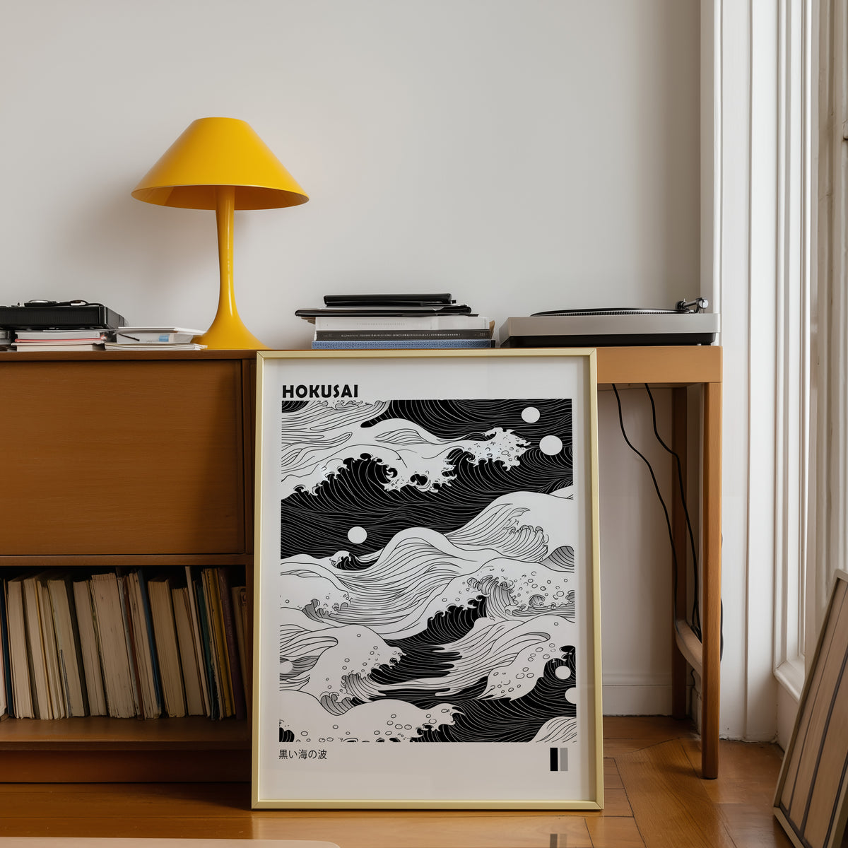 Black sea waves with twin moons print shown in a gold frame below a teak desk with a yellow lamp