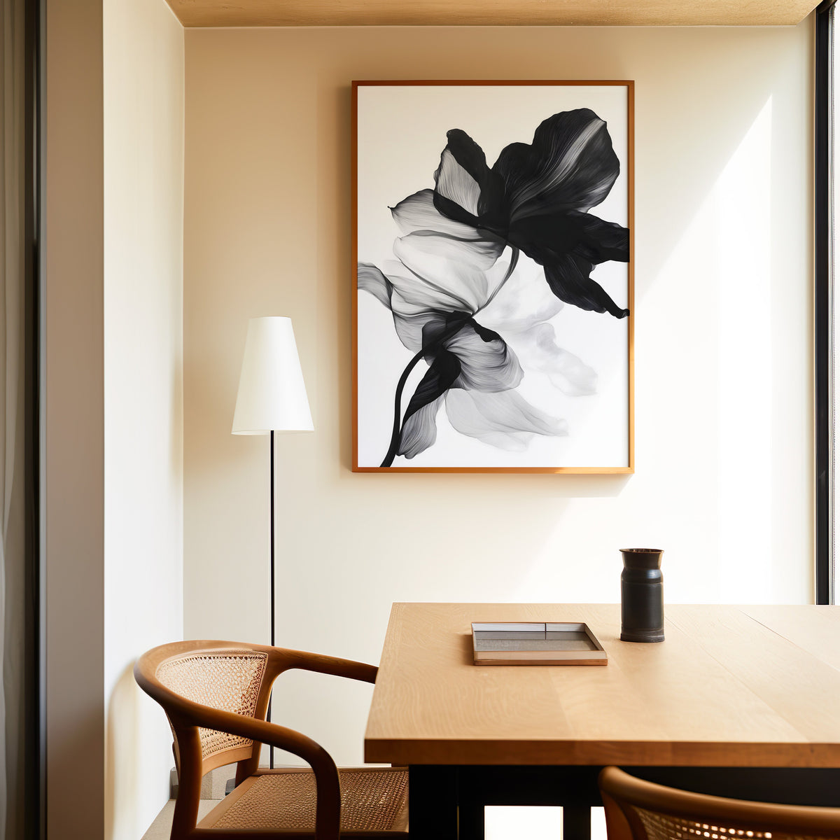 Black and white sheer flower abstract print in a slim oak frame above a dining table with a cane-back chair