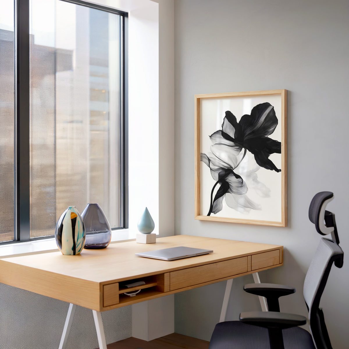 Black and white sheer flower abstract print in a pale wood frame above a home office desk by a tall window