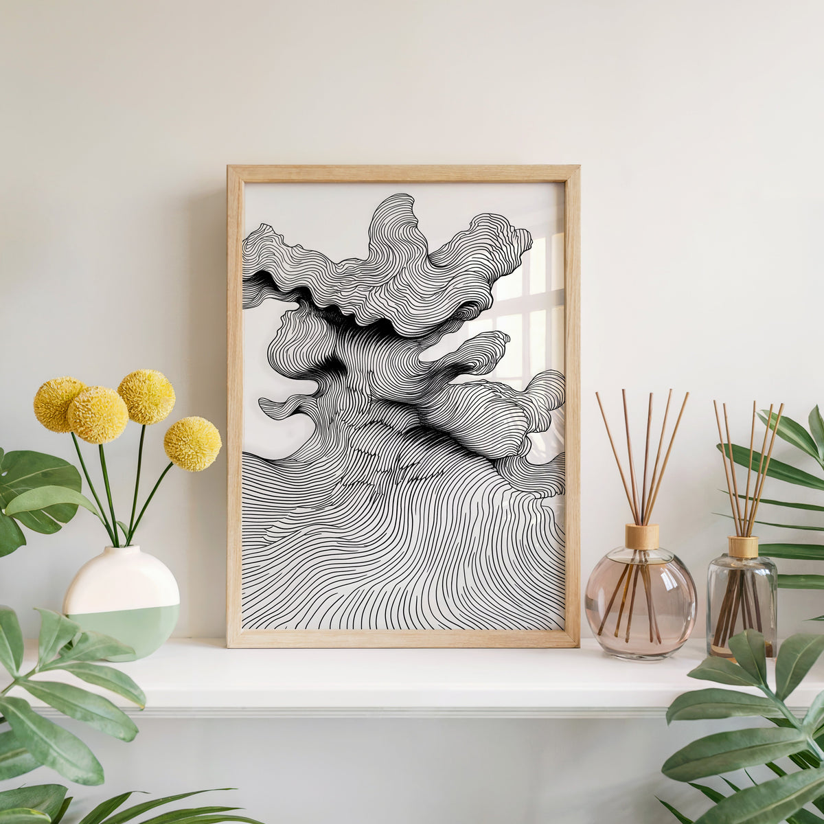 Black and white topographic wave line art print in a light oak frame leaning on a white mantel with yellow flowers