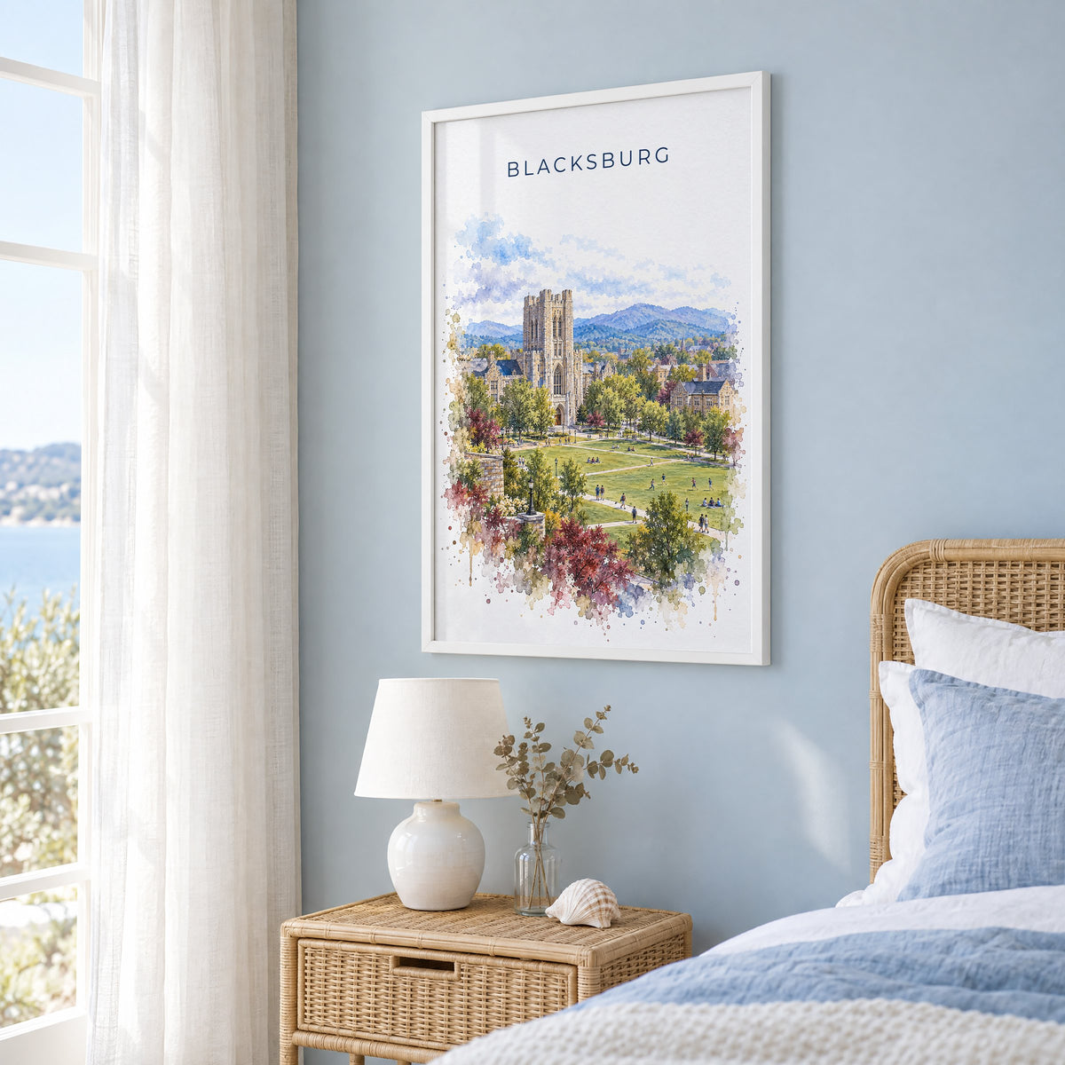Blacksburg watercolor print in a white frame on a pale blue wall beside a rattan bed in a coastal bedroom