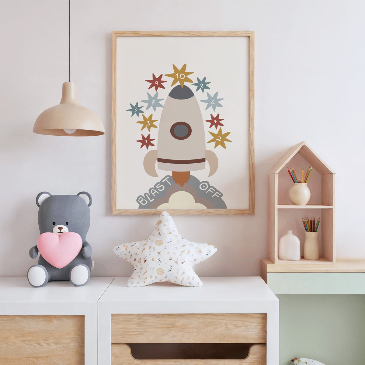 Blast off rocket countdown nursery print in an oak frame above a white dresser with a star pillow and house shelf