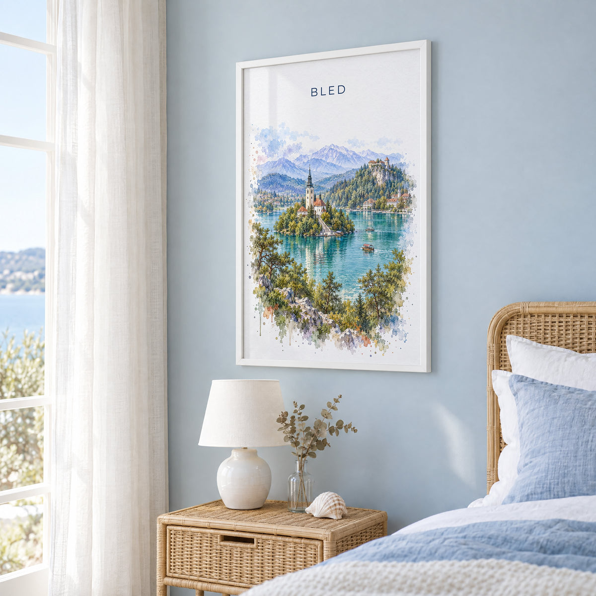 Bled watercolor print in a white frame on a pale blue wall beside a rattan bed in a coastal bedroom