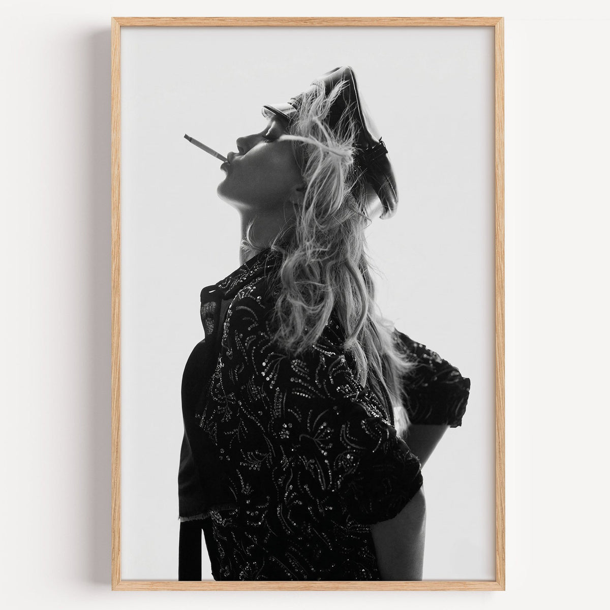 Backlit model in leather cap and sequin jacket print in a light oak frame on a plain white wall