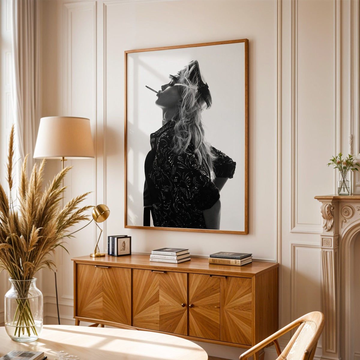 Backlit model in leather cap and sequin jacket print in an oak frame above a sunburst wood sideboard with pampas grass