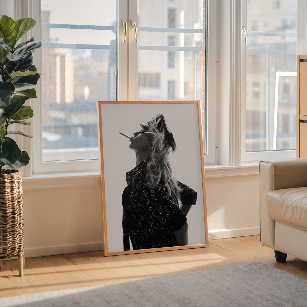 Backlit model in leather cap and sequin jacket print in an oak frame leaning on the floor beside a fiddle leaf fig