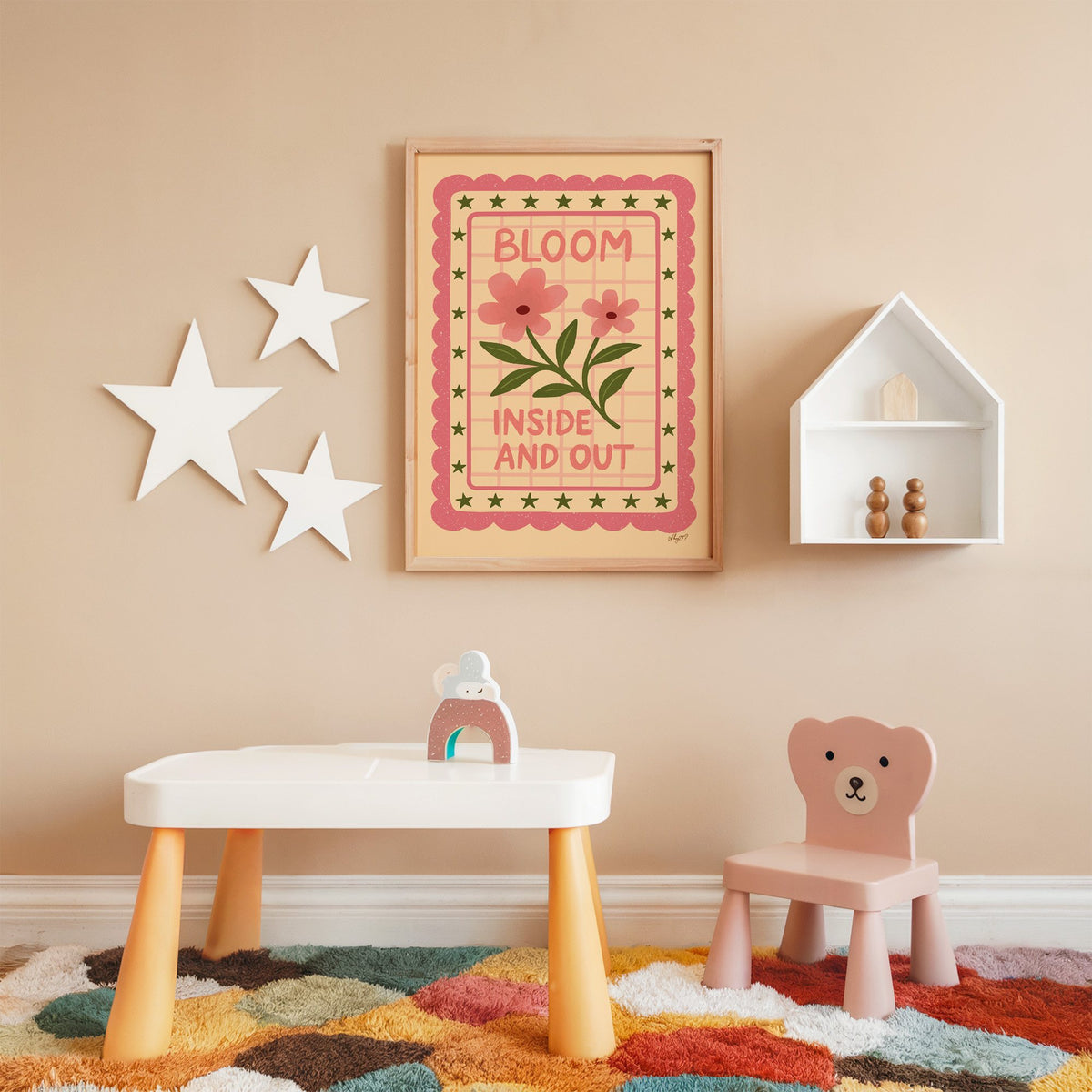 Bloom inside and out pink floral nursery print in an oak frame on a peach wall above a kids table with wall stars