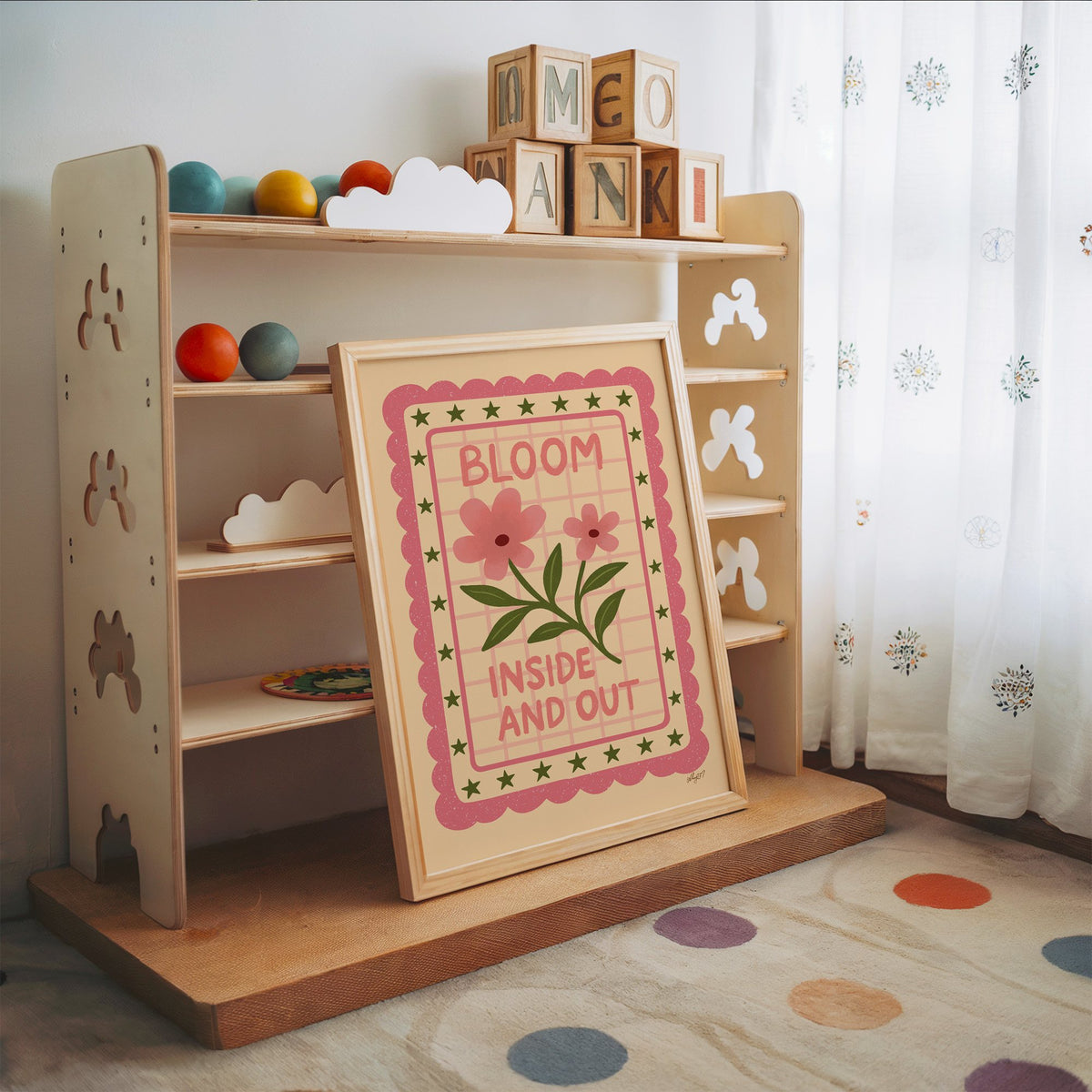 Bloom inside and out pink floral nursery print in an oak frame leaning on a toy shelf with wooden letter blocks
