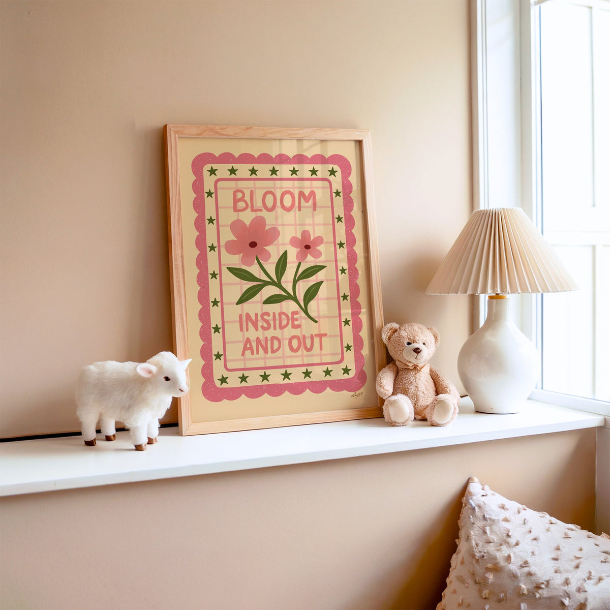 Bloom inside and out pink floral nursery print in an oak frame on a window ledge with a toy lamb and teddy