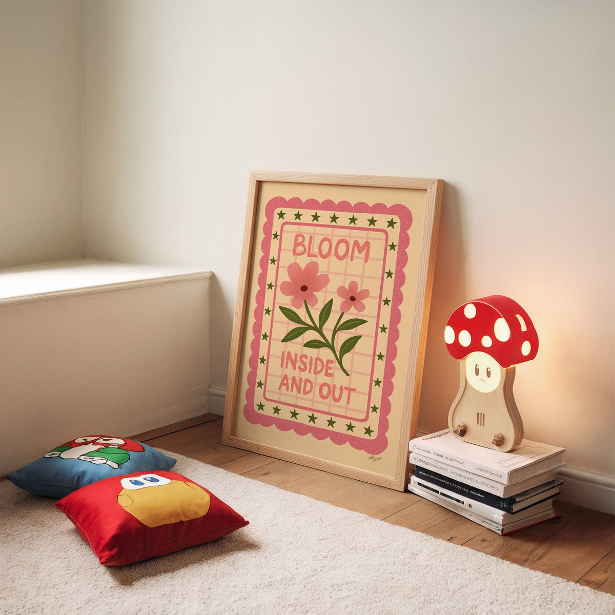 Bloom inside and out pink floral nursery print in an oak frame leaning on a rug beside a mushroom lamp and floor cushions