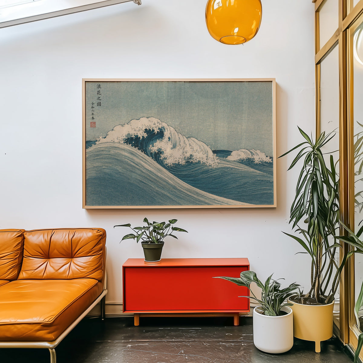 Blue crashing wave woodblock print in a light wood frame above a red cabinet beside a tan leather daybed