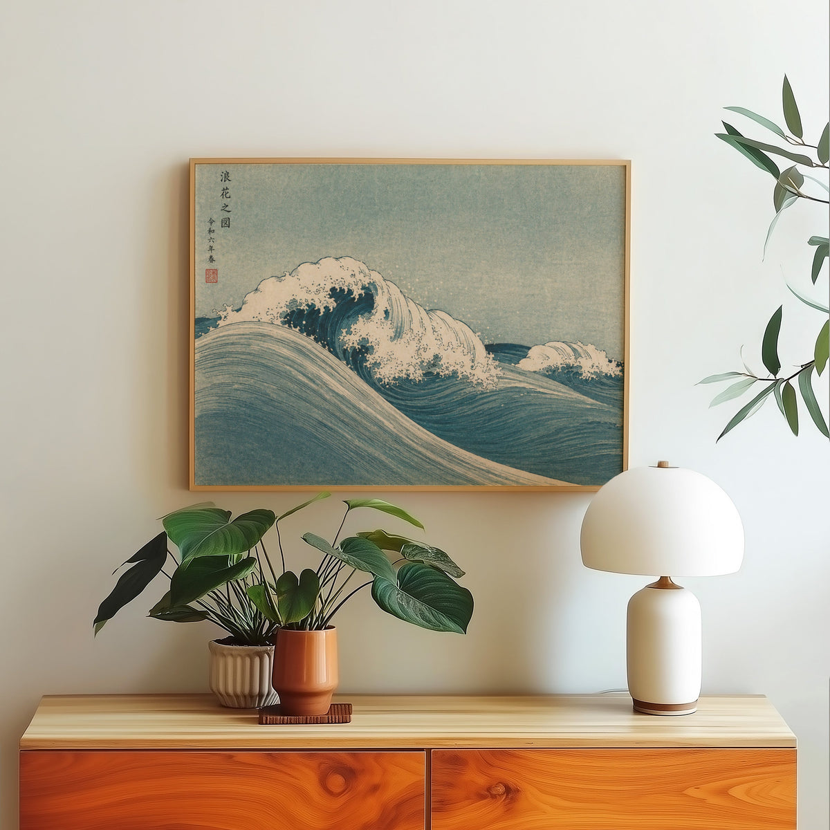Blue crashing wave woodblock print in a light oak frame above a wood sideboard with a white dome lamp
