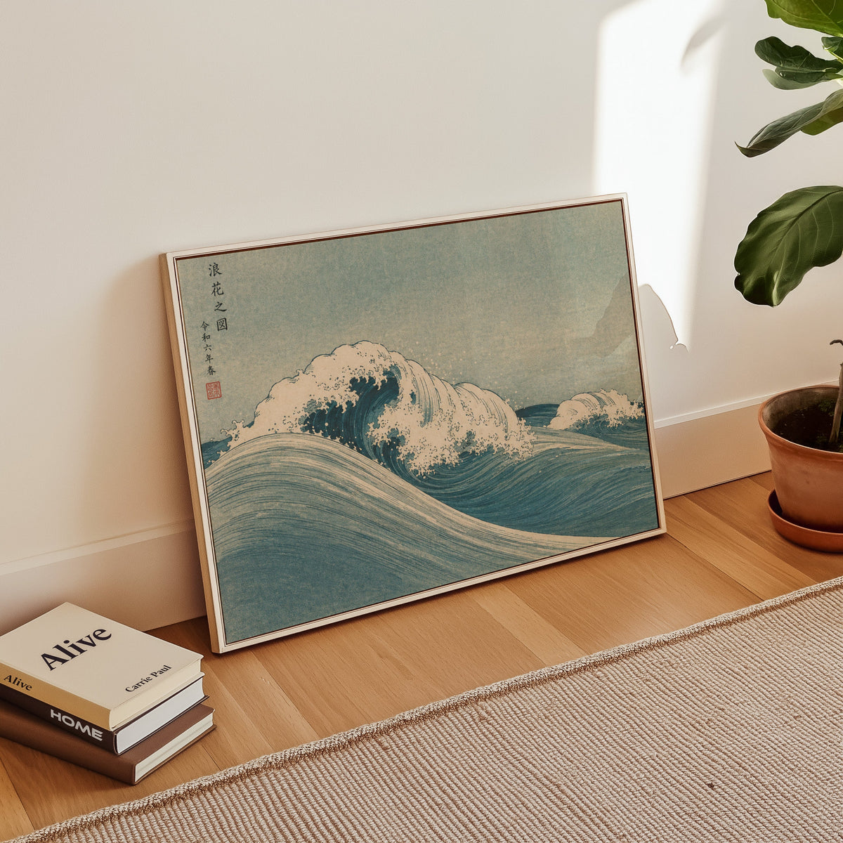 Blue crashing wave woodblock print in a white floater frame leaning on a wood floor beside stacked books