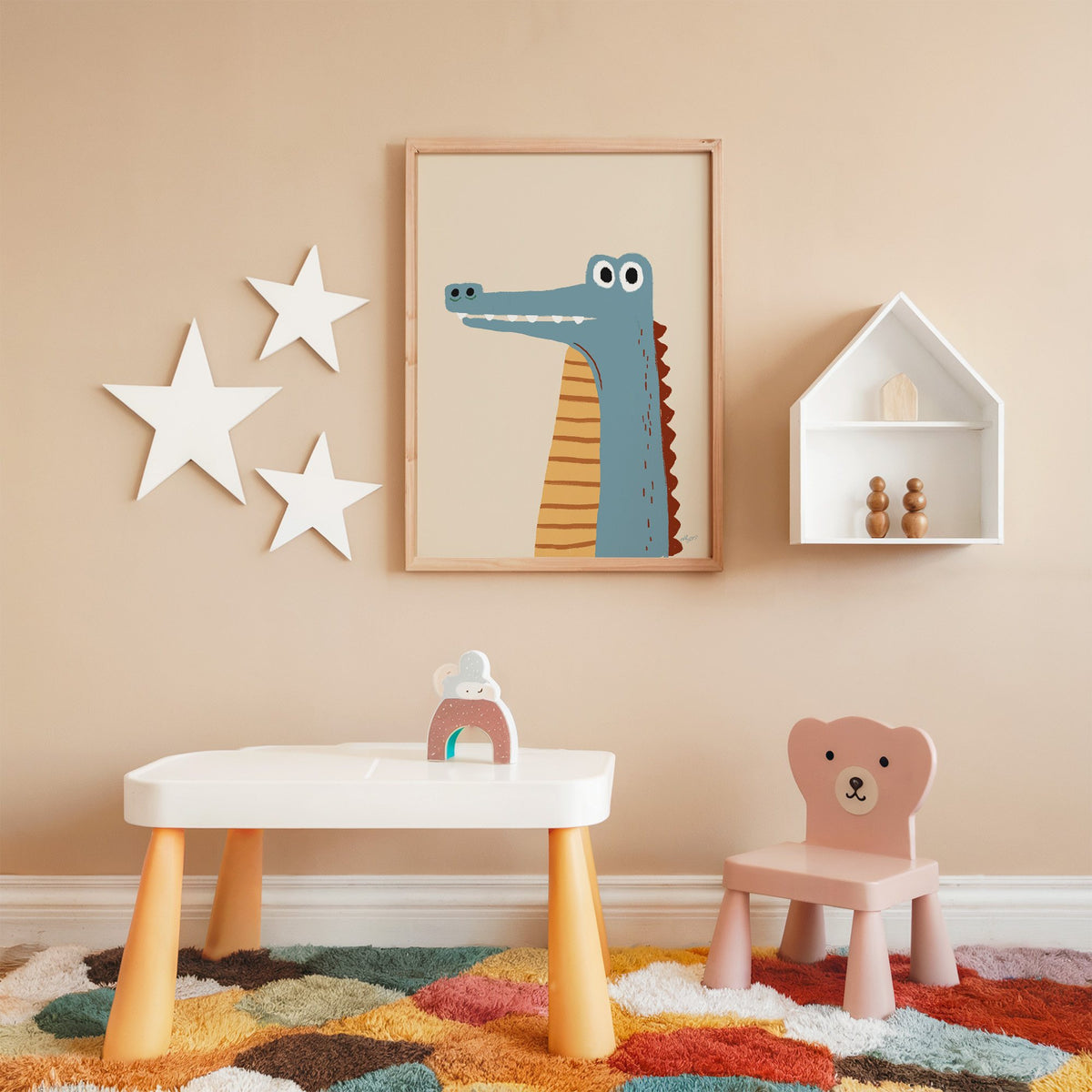 Upright blue crocodile on cream nursery print in an oak frame on a peach wall above a kids table with wall stars