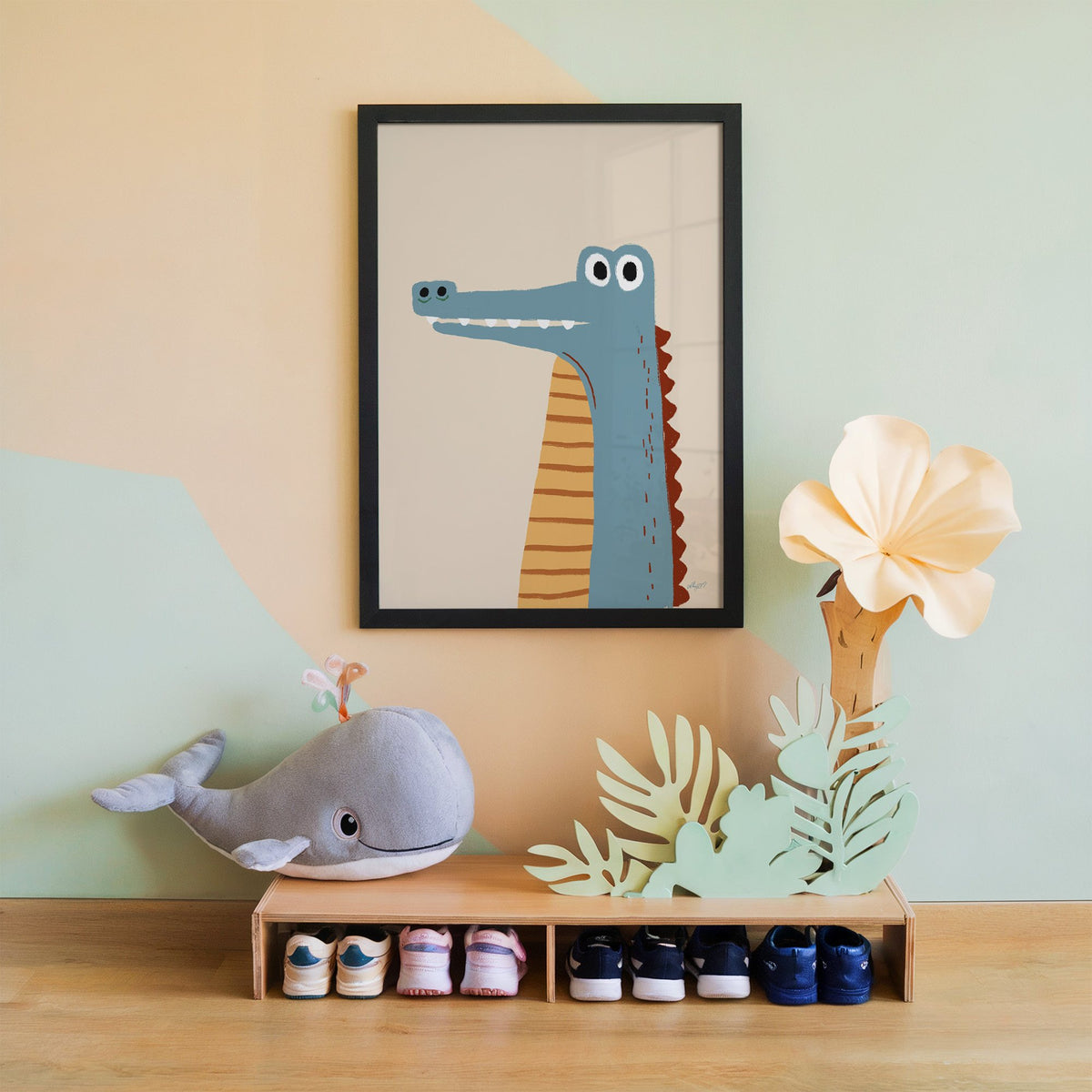 Upright blue crocodile on cream nursery print in a black frame on a mint and peach wall above a whale plush