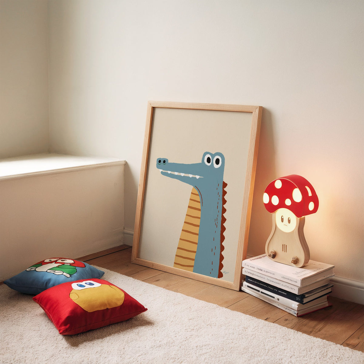 Upright blue crocodile on cream nursery print in an oak frame leaning on a rug beside a mushroom lamp and floor cushions