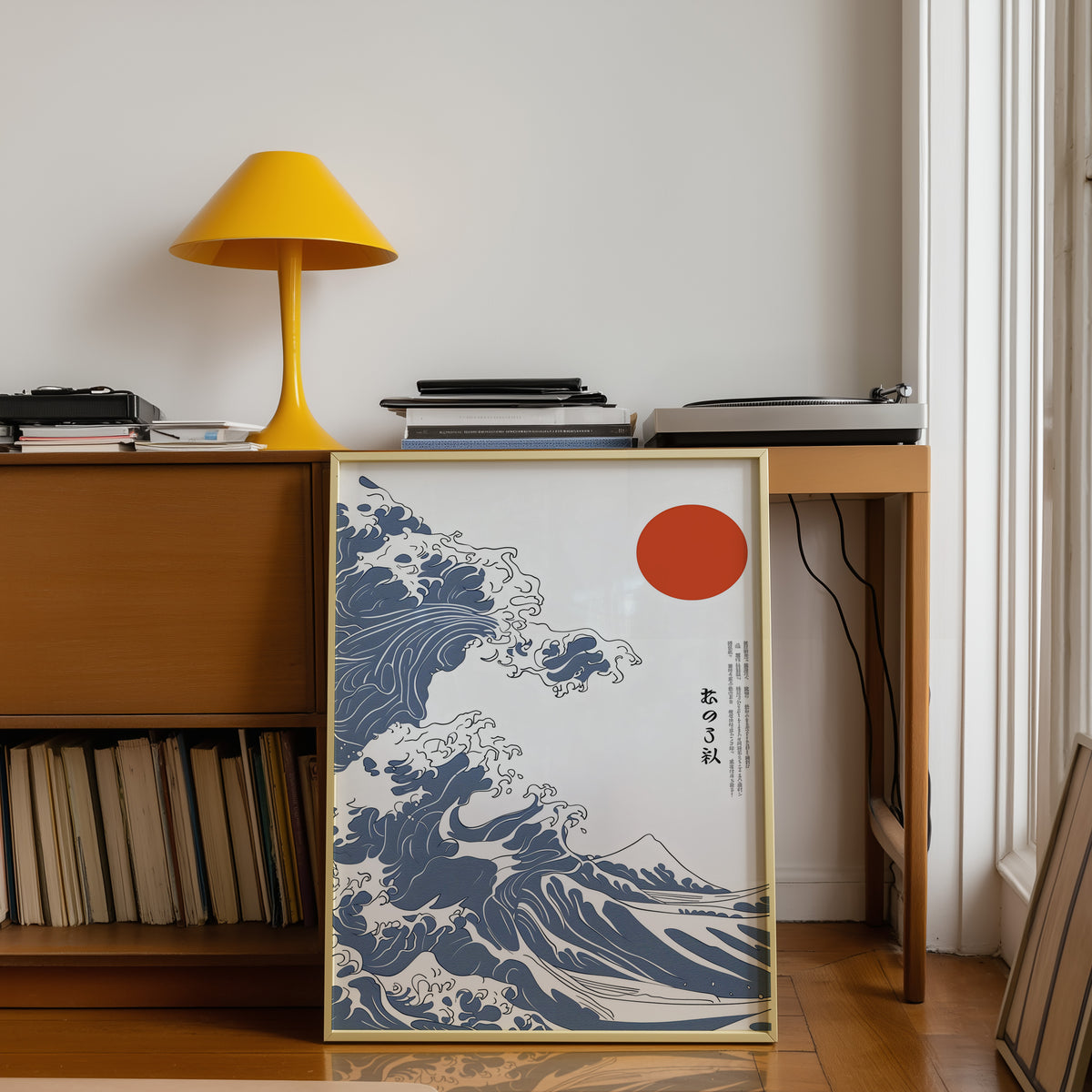 Blue Great Wave with red sun print shown in a gold frame below a teak desk with a yellow lamp