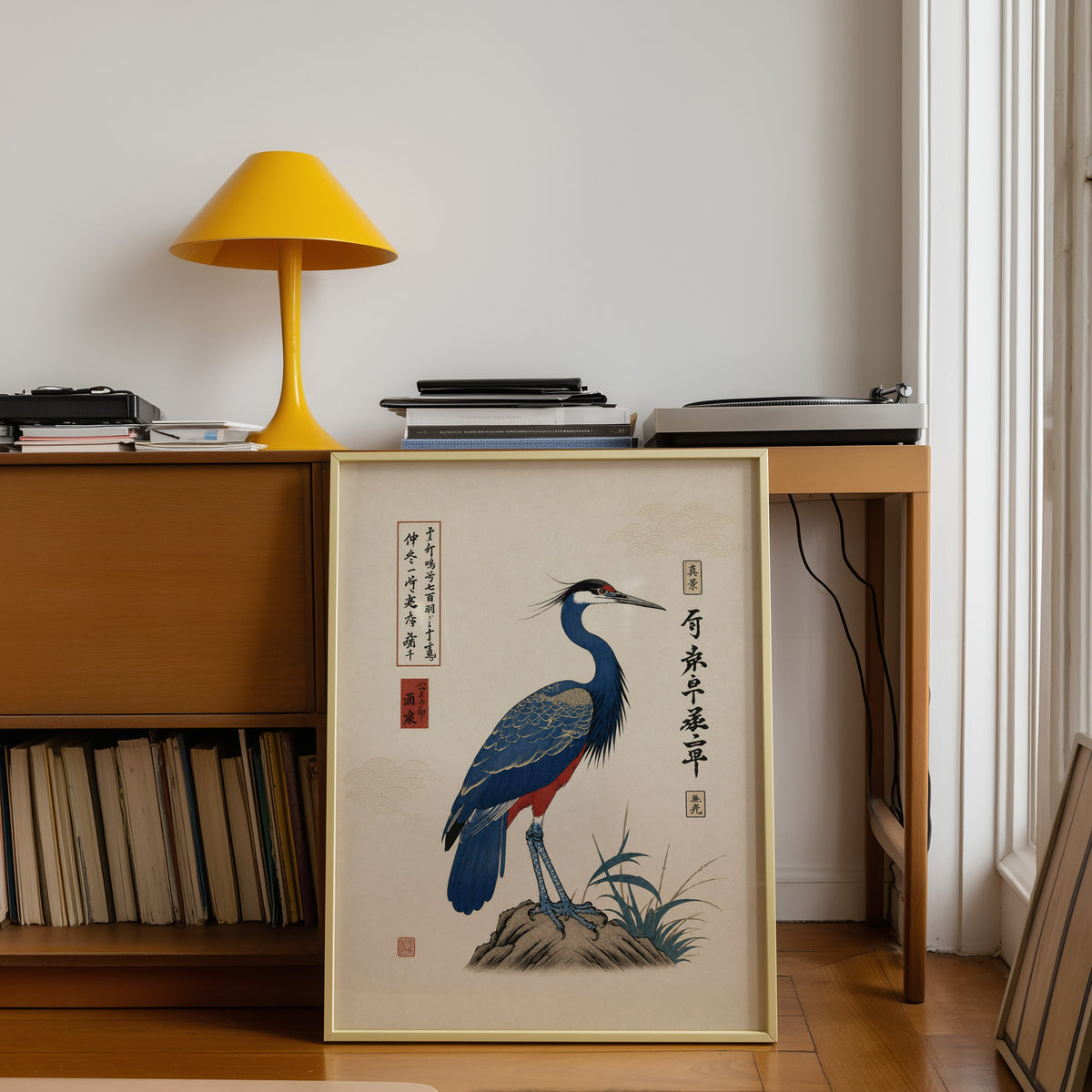Blue crested bird on rock poster shown in a gold frame leaning under a teak desk with a yellow lamp