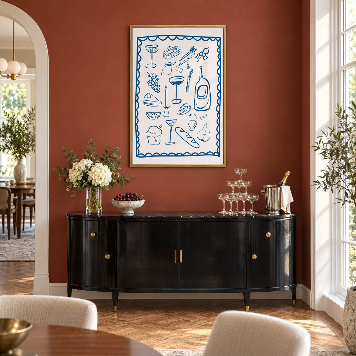 Blue line dinner party scalloped print in a brass frame on a terracotta wall above a black buffet with a champagne tower