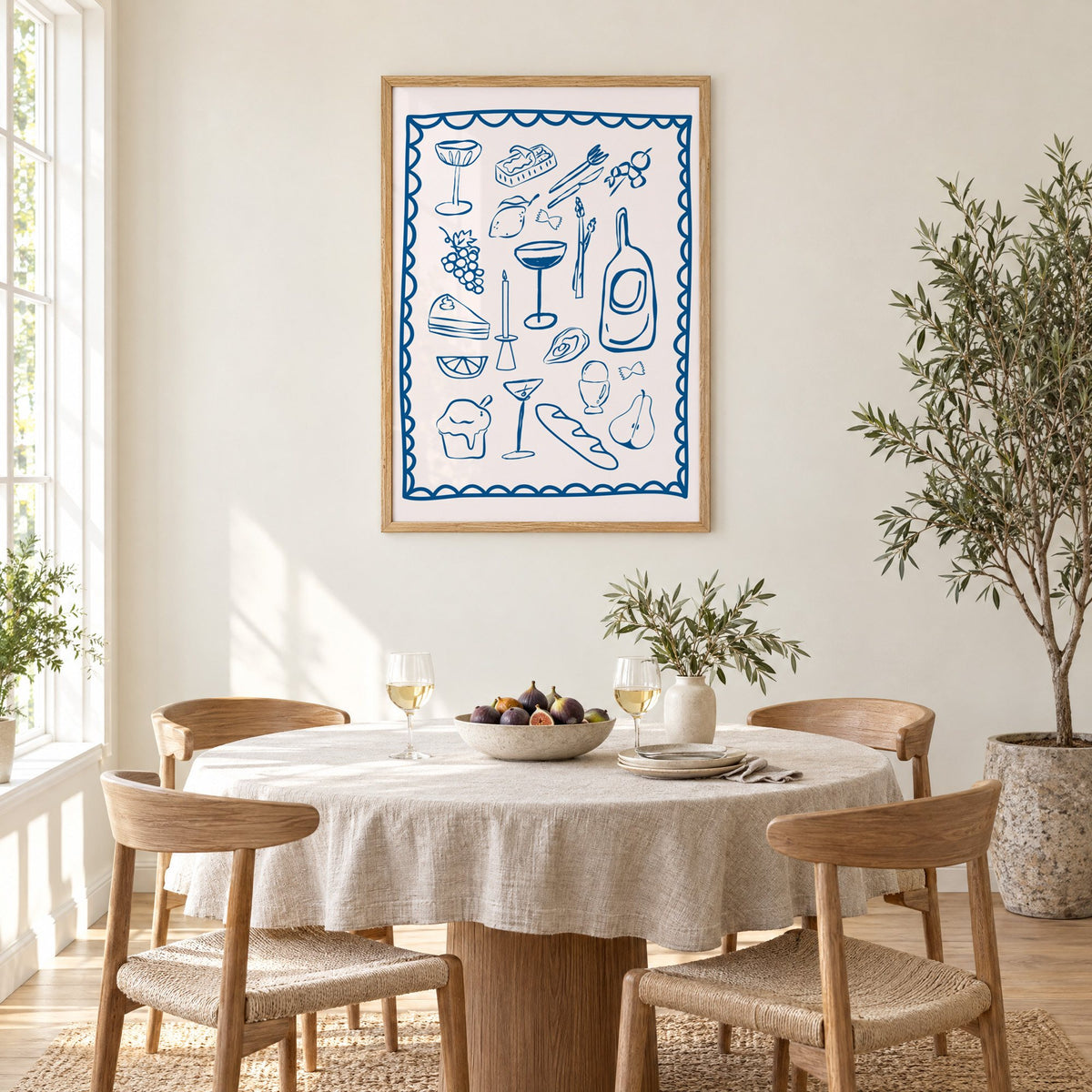 Blue line dinner party scalloped print in an oak frame above a round linen-covered dining table with figs and wine
