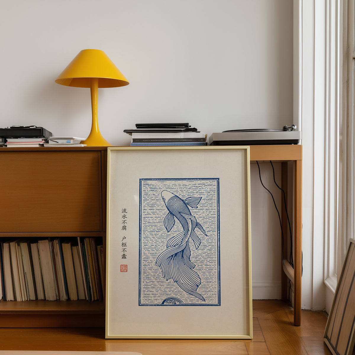 Blue line koi flowing water poster shown in a gold frame leaning under a teak desk with a yellow lamp
